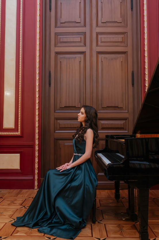 Seated in a teal gown beside the piano